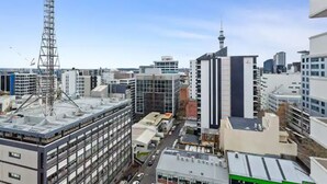 A cityscape with modern buildings, including a tall communication tower and a prominent skyscraper with a spire. - Central City 1Br Apartment (Auckland)