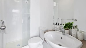 A modern bathroom with a glass shower enclosure, a white sink, and a toilet. - Central City 1Br Apartment (Auckland)