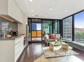 A modern apartment with a kitchen, a living area with a sofa and coffee table, and large windows offering a city view. - Central 2 BR apt - large balcony by Zodiak Stays (Auckland)
