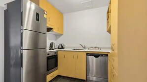 A compact kitchen with a stainless steel refrigerator, a dishwasher, and a stove.