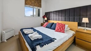A modern bedroom with a large bed, a window, a radiator, and a nightstand with a lamp.