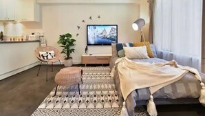 Una moderna camera d'hotel con un letto, un piccolo angolo salotto, una televisione e un angolo cottura sullo sfondo.
