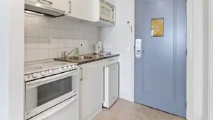 Une cuisine compacte avec des meubles blancs, un four encastré, un four à micro-ondes et un petit réfrigérateur.