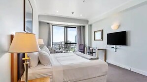 Une chambre d’hôtel moderne dotée d’un grand lit, d’un bureau, d’une chaise, d’une télévision et d’un balcon offrant une vue sur la ville.