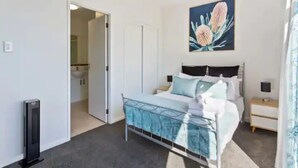A bedroom with a bed, bedside tables, a nightstand, a door, and a painting on the wall. - Stunning Sky Tower View Studio Pool And Gym! (Auckland)