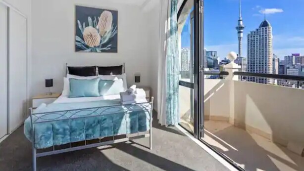 A hotel room with a bed, a painting, and a city view. - Stunning Sky Tower View Studio Pool And Gym! (Auckland)