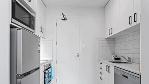 A modern kitchen with white cabinets, a stainless steel refrigerator, a microwave, a dishwasher, and a tiled backsplash. - Stunning Sky Tower View Studio Pool And Gym! (Auckland)