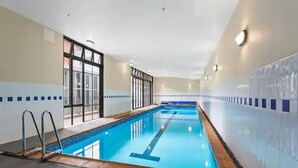 An indoor swimming pool with clear blue water, surrounded by walls with a tiled pattern. - Stunning Sky Tower View Studio Pool And Gym! (Auckland)