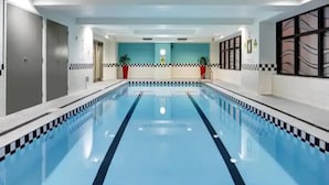 A swimming pool with a checkered border, a blue wall with a plant, and a red chair.