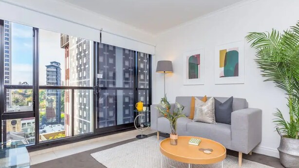 A modern living room with a grey sofa, a round coffee table, and a large window offering a city view.