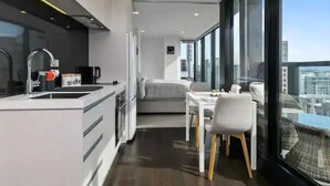 Una cucina moderna con lavello, fornello e frigorifero. C'è un'area pranzo con tavolo e sedie. La stanza ha ampie finestre che offrono vista sulla città.