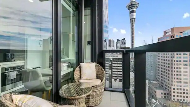 Un balcone con mobili in vimini, una porta vetrata e vista sulla città, inclusa una torre.