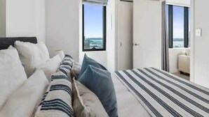 A modern hotel room with a bed, a view of the sea, and a door leading to a balcony. - Sky Tower Views | 2 Bed 2 Bath CBD | Zodiak Stays (Auckland)