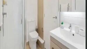 A modern bathroom with a glass-enclosed shower, a toilet, and a vanity with a mirror and sink. - Sky Tower Views | 2 Bed 2 Bath CBD | Zodiak Stays (Auckland)