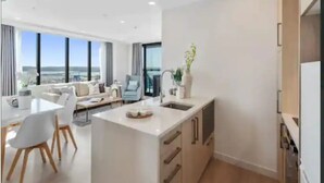 A modern interior with a kitchen, dining area, and a view of the city. - Sky Tower Views | 2 Bed 2 Bath CBD | Zodiak Stays (Auckland)