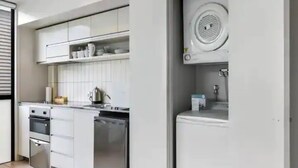 A modern kitchen with white cabinetry, a built-in oven, and a dishwasher. - Lovely And Cozy Apartment - Parking, Pool And Gym! (Auckland)