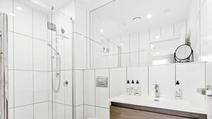 A modern bathroom with a glass shower enclosure, a toilet, and a vanity with a mirror and toiletries. - Convenient Modern 2-Bedroom Unit With Free Parking (Auckland)