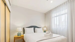 A hotel room with a large bed, two bedside tables with lamps, and sheer curtains on the window. - Convenient Modern 2-Bedroom Unit With Free Parking (Auckland)