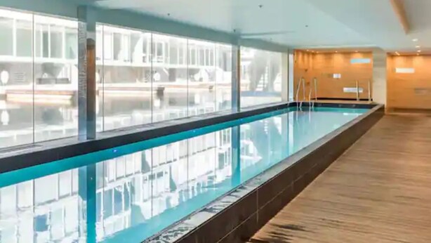 A long indoor swimming pool with glass walls, wooden flooring, and a clear view of the adjacent building. - Wynyard Viaduct Harbour 2BR+Parking: Zodiak Stays (Auckland)