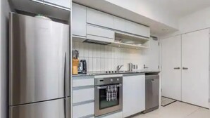 A modern kitchen with stainless steel appliances, white cabinetry, and a tiled backsplash. - Wynyard Viaduct Harbour 2BR+Parking: Zodiak Stays (Auckland)