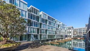 A modern building with a glass facade and a swimming pool in the foreground. - Wynyard Viaduct Harbour 2BR+Parking: Zodiak Stays (Auckland)