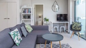 A modern living room with a grey sofa, a round coffee table, a TV, and a bookshelf. - Wynyard Viaduct Harbour 2BR+Parking: Zodiak Stays (Auckland)