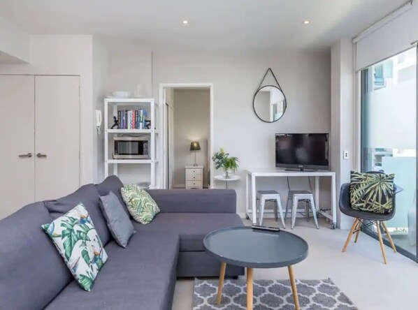 A modern living room with a grey sofa, a round coffee table, a TV, and a bookshelf. - Wynyard Viaduct Harbour 2BR+Parking: Zodiak Stays (Auckland)
