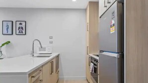 A modern kitchen with a refrigerator, microwave, and wooden cabinets. - Stunning 2BR w/ Views Near Sky Tower- Zodiak Stays (Auckland)