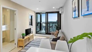 A modern living room with a sofa, a TV, and a large window offering a view of the sea. - Stunning 2BR w/ Views Near Sky Tower- Zodiak Stays (Auckland)