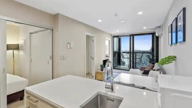 A modern kitchen with a large island, a dining area with a view, and a balcony with a cityscape. - Stunning 2BR w/ Views Near Sky Tower- Zodiak Stays (Auckland)