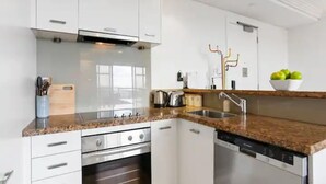 A modern kitchen with white cabinets, stainless steel appliances, and a granite countertop. - Bright 1 Bedroom Beauty with Balcony Zodiak Stays (Auckland)