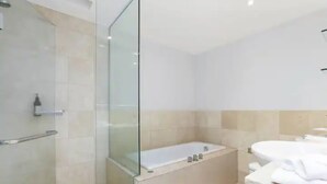 A modern bathroom with a glass-enclosed shower, a freestanding bathtub, and a white vanity with a mirror. - Bright 1 Bedroom Beauty with Balcony Zodiak Stays (Auckland)