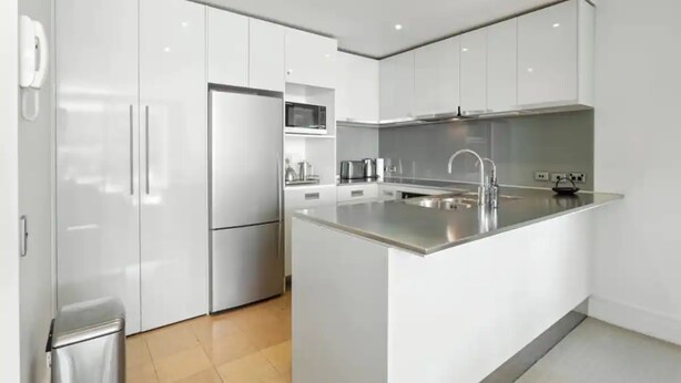 A modern kitchen with white cabinetry, a stainless steel refrigerator, a microwave, and a sink with a faucet. - Gorgeous 2BR in Wynyard Quarter by Zodiak Stays (Auckland)