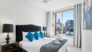 A modern hotel bedroom with a large bed, a ceiling fan, and a city view through the window. - Gorgeous 2BR in Wynyard Quarter by Zodiak Stays (Auckland)