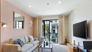 En moderne stue med sofa, sofabord, fjernsyn og en balkon med udsigt til bygninger.