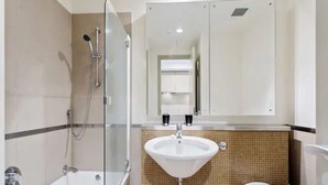 Et moderne badeværelse med et glasafskærmet brusebad, en hvid vask og et toilet.