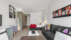 A modern hotel room with a flat-screen TV, a sofa, a red accent wall, and a bed with white linens. - Stunning Spacious Studio In Viaduct Basin (Auckland)