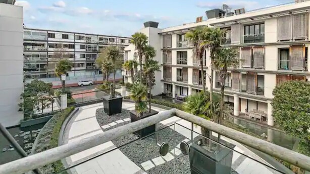 A multi-story residential building with balconies, a paved courtyard, and a view of a street with parked cars. - Stunning Spacious Studio In Viaduct Basin (Auckland)