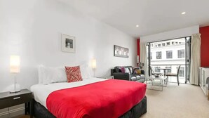 A modern hotel room with a large bed, a desk, a sofa, and a balcony with a view of the city. - Stunning Spacious Studio In Viaduct Basin (Auckland)