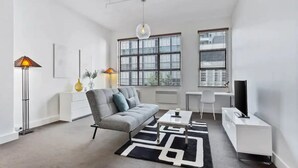 A modern living room with a grey sofa, a black and white rug, a standing lamp, and a TV on a white stand. - Stylish studio near Spark Arena I Zodiak Stays (Auckland)