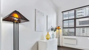 A modern interior with a white console, a floor lamp, and a window with blinds. - Stylish studio near Spark Arena I Zodiak Stays (Auckland)