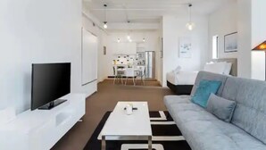 A modern living room with a flat-screen TV, a grey sofa with a teal pillow, a white coffee table, and a black and white rug. - Stylish studio near Spark Arena I Zodiak Stays (Auckland)