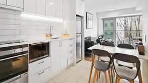 A modern kitchen with white cabinetry, a built-in oven, and a dining area with a table and chairs. - Central Modern Apt. w/ Working Space Zodiak Stays (Auckland)
