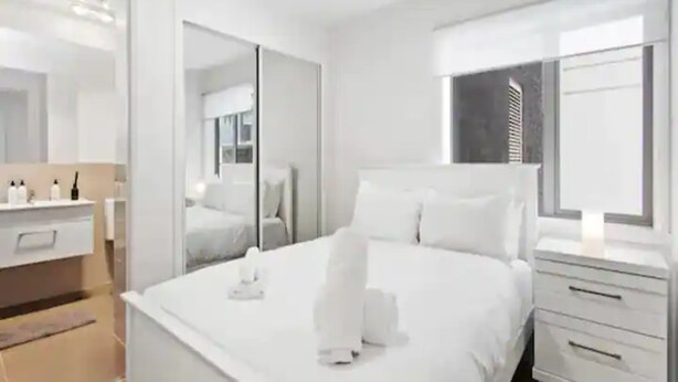 A modern hotel room with a large bed, a bedside table, a mirror, and a window with blinds. - Central Modern Apt. w/ Working Space Zodiak Stays (Auckland)