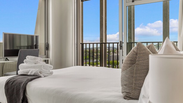 A hotel room with a bed, a desk with a computer, and a window with a city view.