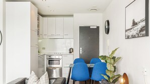 A compact kitchen with white cabinets, a built-in oven, and a dining area with blue chairs.