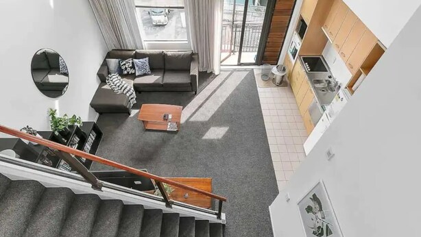 A modern apartment with a staircase, a living room with a sofa and coffee table, and a kitchen area.