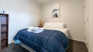 A bedroom with a bed, a bedside table, a lamp, a shelf, and a framed picture on the wall.