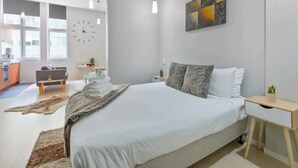Un dormitorio moderno con una cama grande, un escritorio y vista a la cocina.