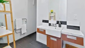 Un baño moderno con un lavamanos blanco, espejo y estante de madera con una planta.